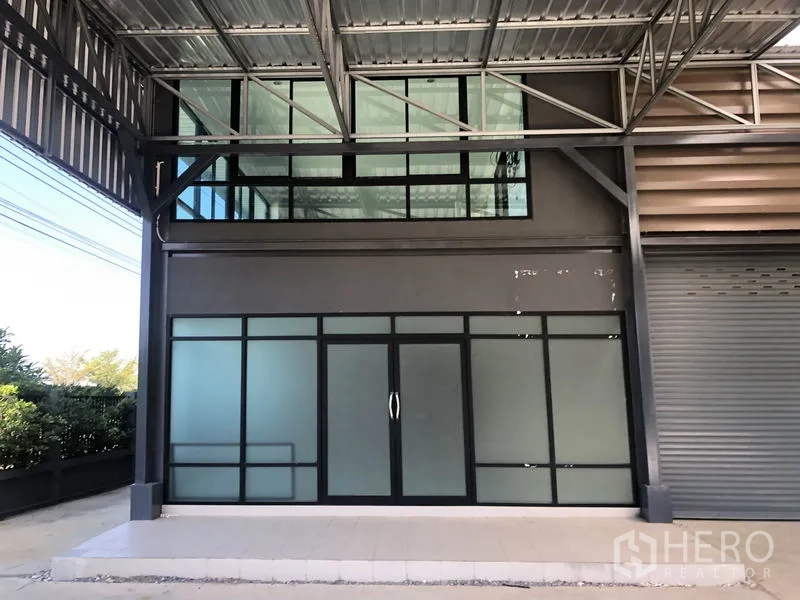 工厂 出租或出售在Bang Bo, Samut Prakan - 一层玻璃办公室入口，位于金属雨棚与夹层窗户下方。