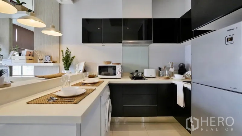 Condominium for rent or sale in Khlong Toei, Bangkok - Modern U-shaped kitchen with glossy black cabinets, white counters, stove, microwave and fridge.