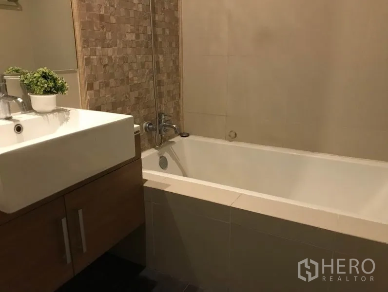 Condominium for rent or sale in Watthana, Bangkok - Modern bathroom with square vanity and a tiled bathtub with shower mixer.