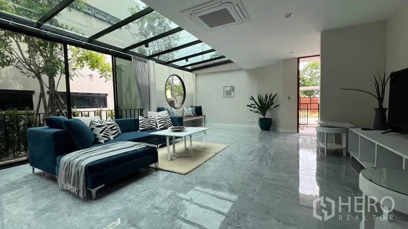 บ้าน ให้เช่าในLat Krabang, Bangkok - โถงนั่งเล่นพร้อมโซฟาสีน้ำเงิน หน้าต่างวงกลม และกันสาดกระจกมองสวน