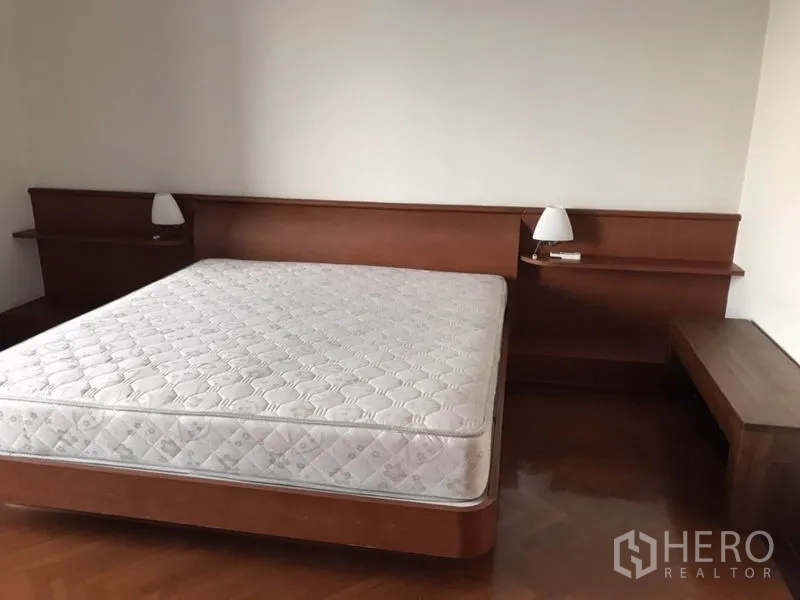 Condominium for rent or sale in Watthana, Bangkok - Master bedroom with king-size bed, wooden headboard and bedside lamps.