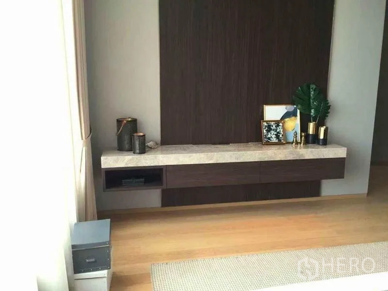 公寓 出租在Bang Rak, Bangkok - 卧室内悬浮式电视柜，石面台与装饰品，浅色木地板。
