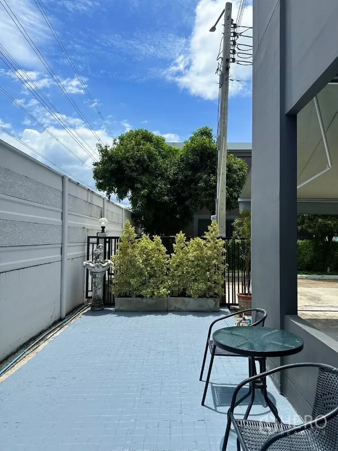 Townhouse for rent in Bang Phli, Samut Prakan - Front patio with blue tiled terrace, black metal gate, potted shrubs and outdoor bistro set.