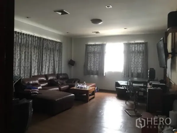 Warehouse for rent in Khlong Sam Wa, Bangkok - Staff lounge with brown leather sectional sofa, curtains, wood flooring and a wall-mounted TV.