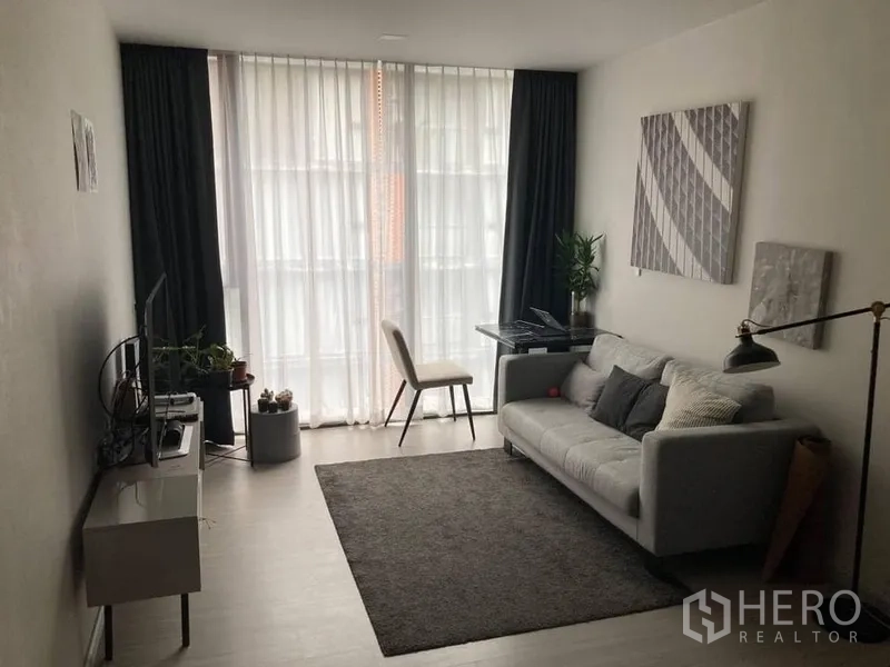 公寓 出租在Khlong Toei, Bangkok - 曼谷公寓客厅采光充足，灰色沙发、书桌与落地窗帘。