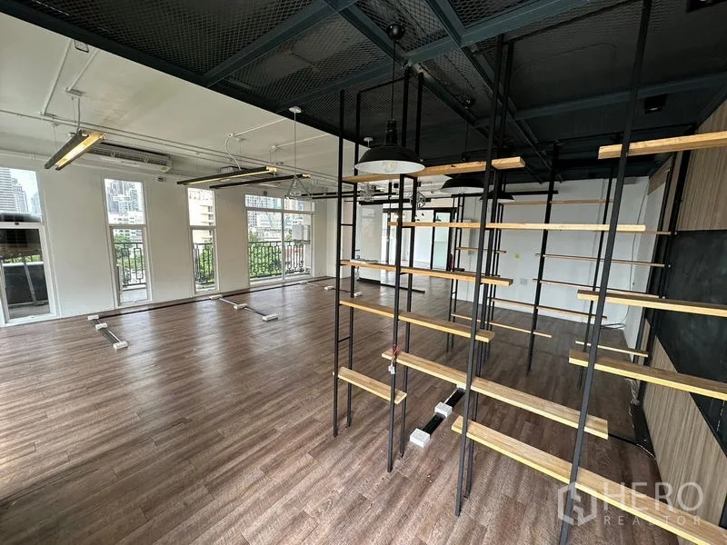 办公空间 出租在Watthana, Bangkok - 开放式办公室，金属木质层架分隔，多扇法式窗与栏杆，城市景观。