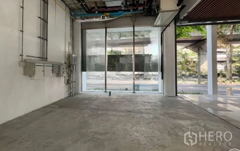 零售空间 出租在Phaya Thai, Bangkok - 一层临街零售铺，水泥地面、外露管线与设备，整面落地玻璃门面朝向街景，位于拍耶泰区。