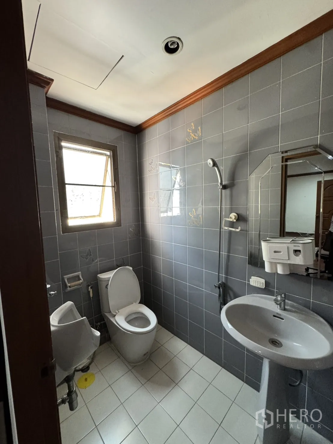 Home Office for rent in Watthana, Bangkok - Compact bathroom with gray tiles, window, pedestal sink, toilet, and urinal.