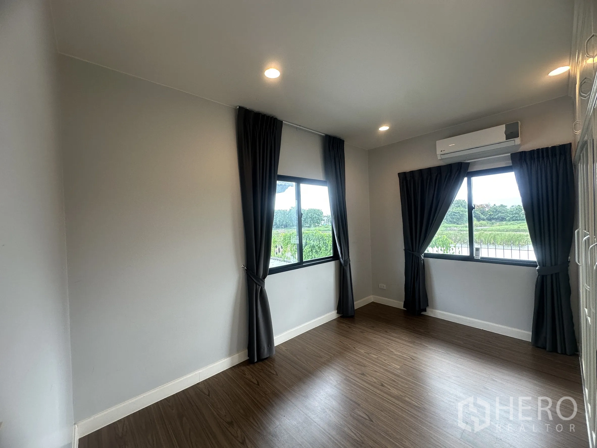 独栋房屋 for rent or sale in Lam Luk Ka, Pathum Thani - 采光充足的卧室，木质地板、深色窗帘与分体空调。