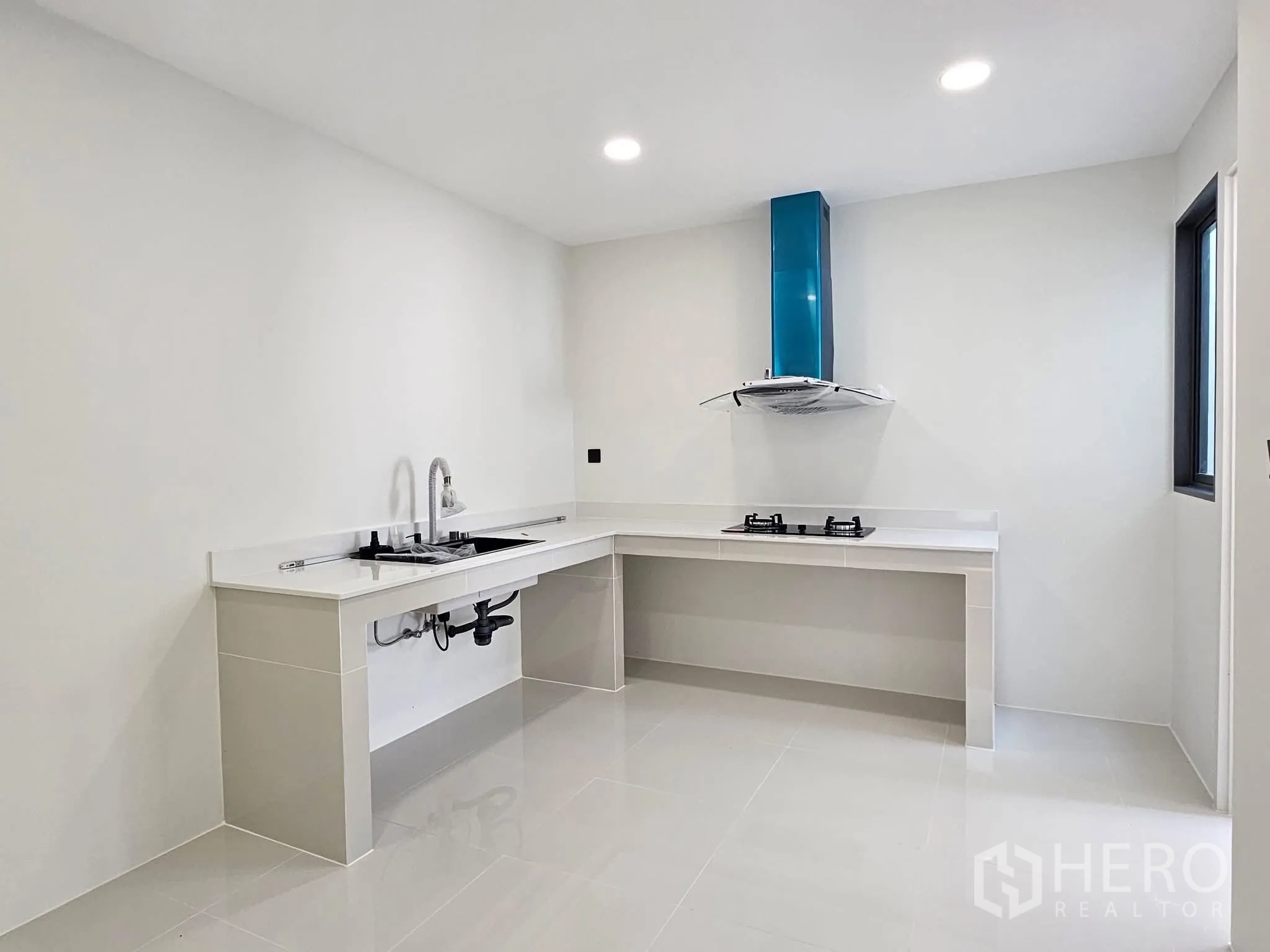 บ้านเดี่ยว for sale in Lat Phrao, Bangkok - ห้องครัวโทนขาว เคาน์เตอร์รูปตัวแอล เตาแก๊ส 2 หัว และเครื่องดูดควัน