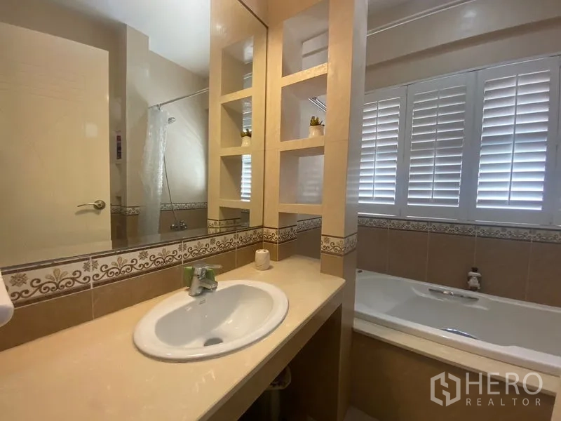 Detached House for sale in Khlong Toei, Bangkok - Bathroom with long vanity, built-in shelving, and bathtub beneath shuttered windows.