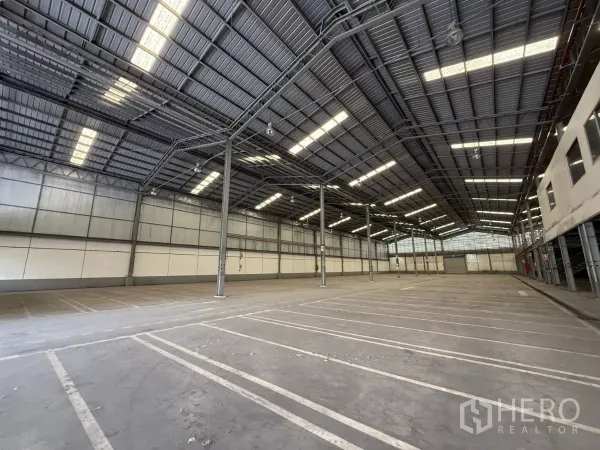 Factory for rent in Lat Krabang, Bangkok - Industrial floor marked for parking and loading, tall insulated walls, steel columns and a roller shutter at the far end.
