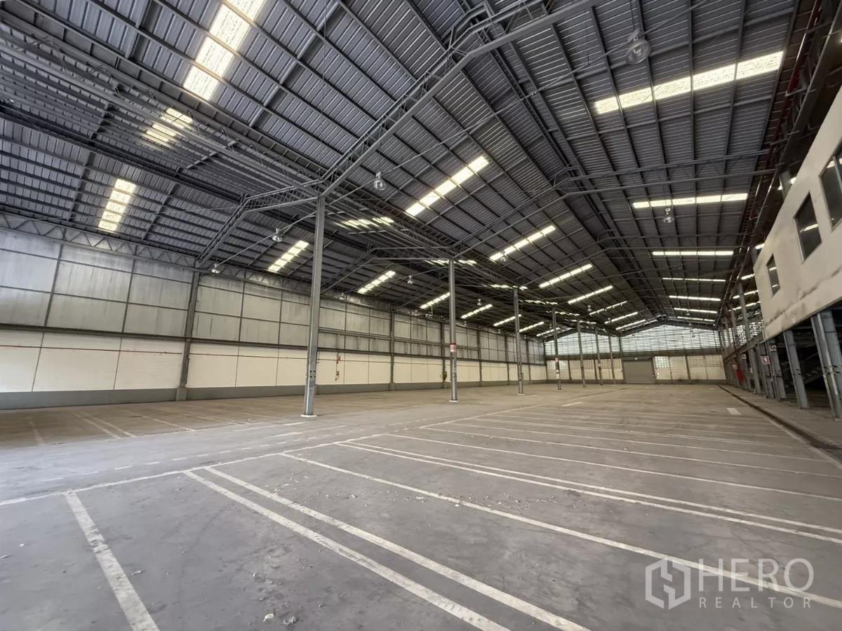 Factory for rent in Lat Krabang, Bangkok - Industrial floor marked for parking and loading, tall insulated walls, steel columns and a roller shutter at the far end.
