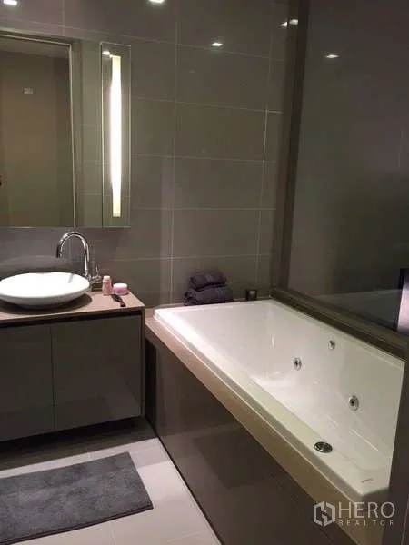 Condominium for rent in Bang Rak, Bangkok - Bathroom featuring a large jacuzzi bathtub beside a vanity with illuminated mirror.