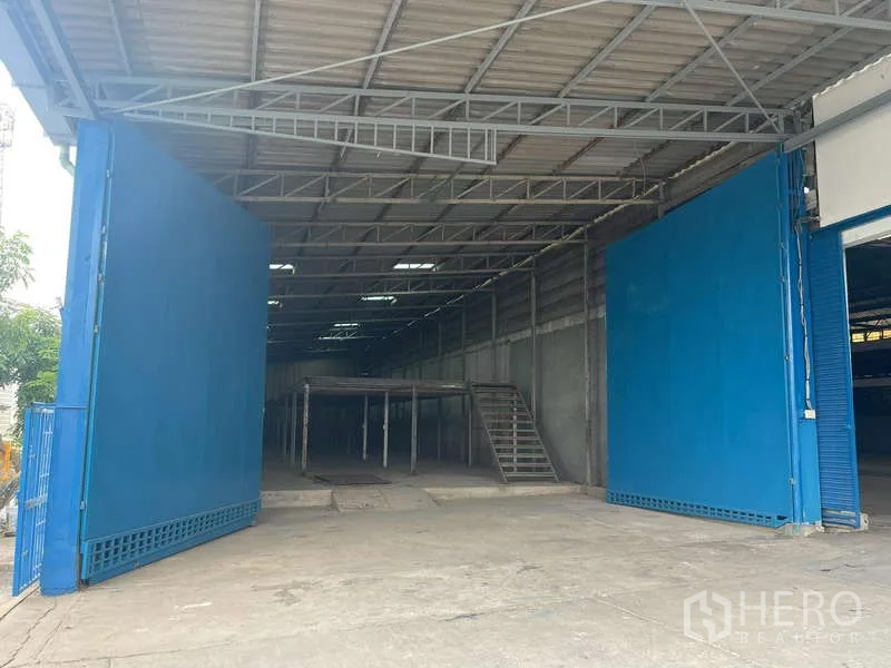 Warehouse for rent in Nong Khaem, Bangkok - Large blue sliding gates opening to a loading area with mezzanine and stairs.