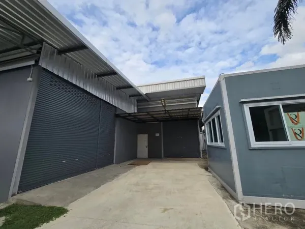 Warehouse for rent in Don Mueang, Bangkok - Entry courtyard with covered loading area and a small detached office beside roller doors.