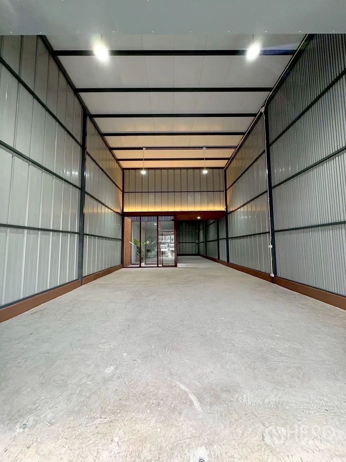 Warehouse for rent in Suan Luang, Bangkok - Long storage area with concrete floor, metal cladding walls and a sliding glass entry to the office.