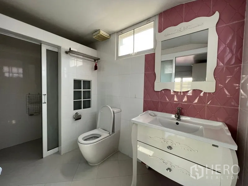 独立式住宅 出租在Bang Kapi, Bangkok - 卫生间配白色梳妆台、粉色点缀墙、坐便器与独立淋浴区。