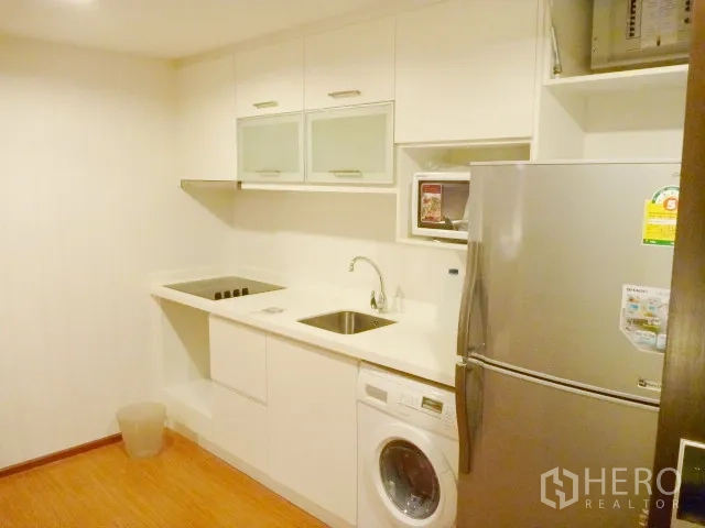 Condominium for rent in Watthana, Bangkok - Compact white kitchen with cooktop, sink, fridge, microwave and front-load washing machine.
