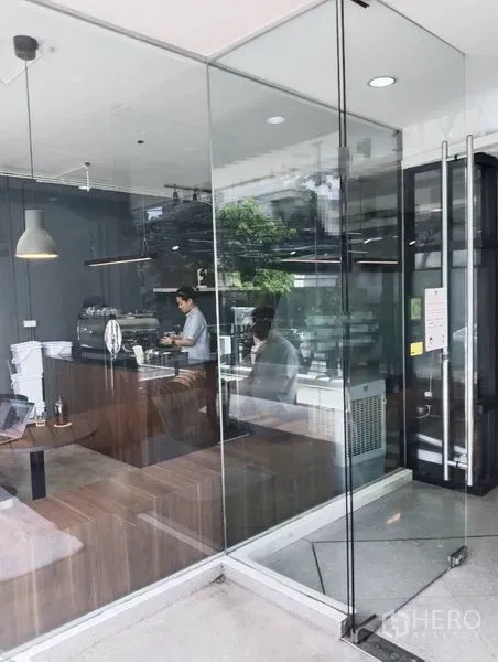 零售空间 出租在Watthana, Bangkok - 落地玻璃商铺内景，木质吧台与吊灯，现代简约风格。