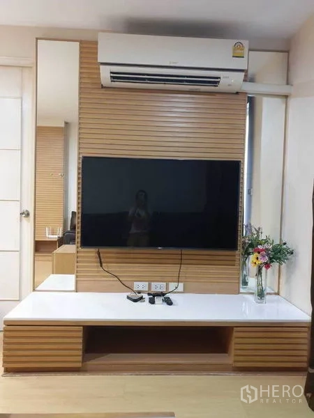 Condominium for rent in Watthana, Bangkok - Living room media wall with mounted flat-screen TV, air conditioner, and built-in low cabinet.