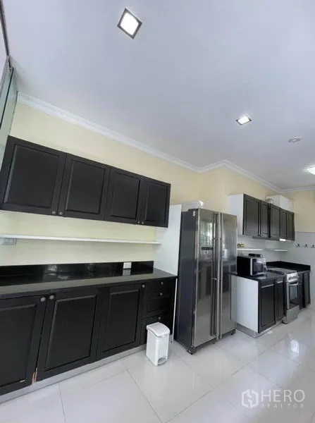 独立式住宅 出租在Prawet, Bangkok - 厨房一侧深色橱柜，双开门冰箱与内置电器。
