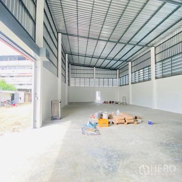 คลังสินค้า ให้เช่าในBang Khae, Bangkok - โกดังเพดานสูง ประตูม้วนทางเข้ากว้าง มีช่องระบายอากาศและวัสดุวางอยู่บนพื้น