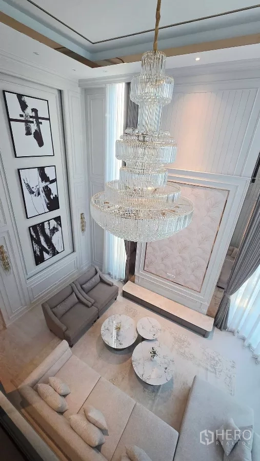 Detached House for rent in Prawet, Bangkok - Aerial view of the grand chandelier above a bright double-height lounge with tall windows.