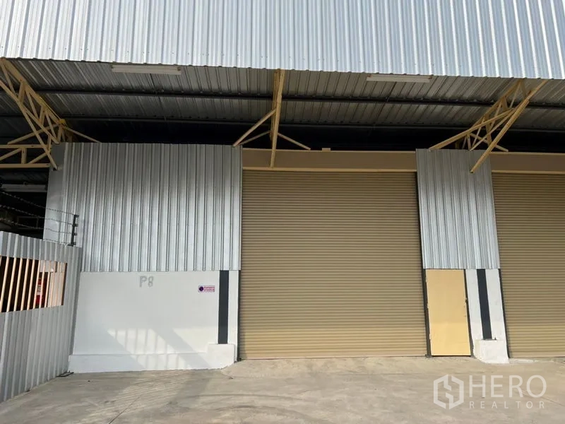 Warehouse for rent in Suan Luang, Bangkok - Metal-clad warehouse exterior with two beige roller shutter doors and a covered loading bay.
