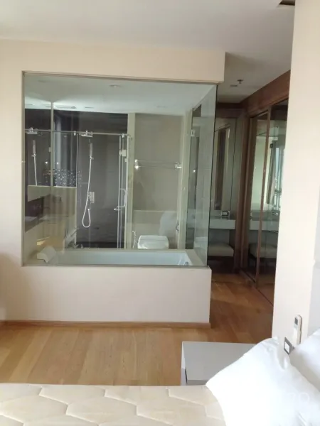 Condominium for rent in Ratchathewi, Bangkok - Master bedroom with a glass-walled bathroom showcasing a bathtub and separate shower on wood flooring.