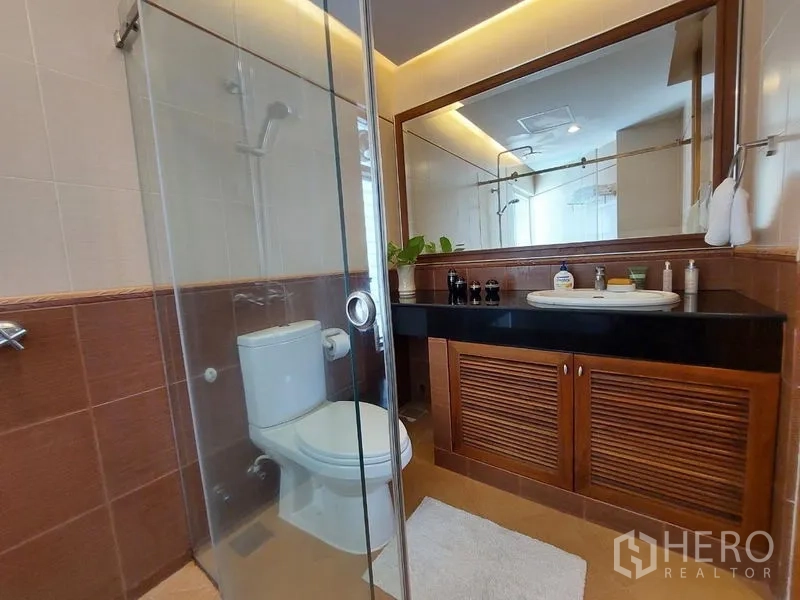 อพาร์ทเมนท์ ให้เช่า - ห้องน้ำพร้อมตู้กระจกกั้นอาบน้ำ โถสุขภัณฑ์ เคาน์เตอร์สีดำ และกระจกบานใหญ่