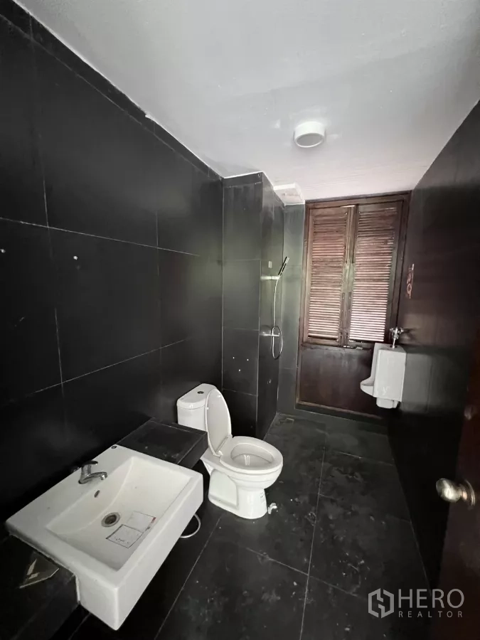 零售空间 出租在Khlong Toei, Bangkok - 黑色瓷砖卫生间，配洗手盆、坐便器和窗户。