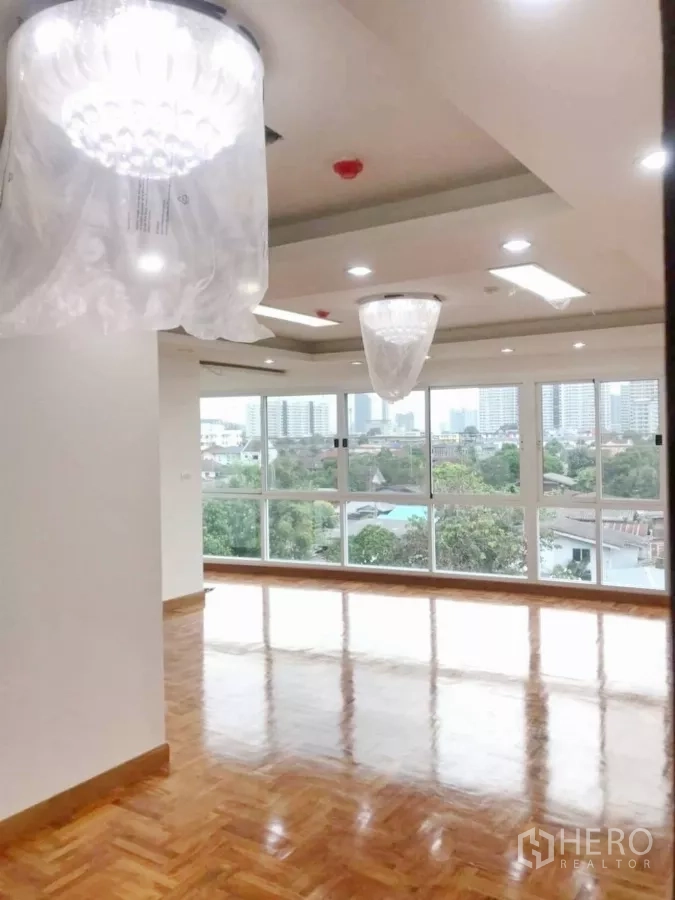 Apartment for sale in Khlong Toei, Bangkok - Spacious hall with parquet floor, ceiling lights and full-height windows overlooking the city.