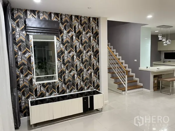 บ้าน ให้เช่าในBang Kapi, Bangkok - โถงรับแขกแบบโอเพ่น พร้อมผนังลายเด่น บันได และมุมมองไปยังครัวโมเดิร์น