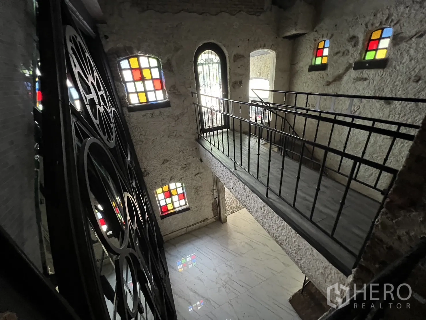 零售空间 出租在Watthana, Bangkok - 上层廊桥，旁有装饰性铁艺屏风与多扇彩色玻璃窗。