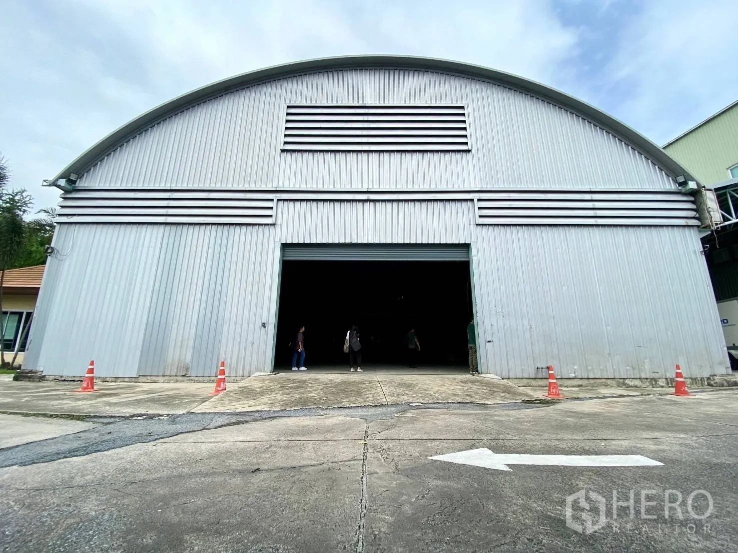 Warehouse for rent in Lak Si, Bangkok - Front view of a metal-clad warehouse with a large roller shutter door and paved driveway.