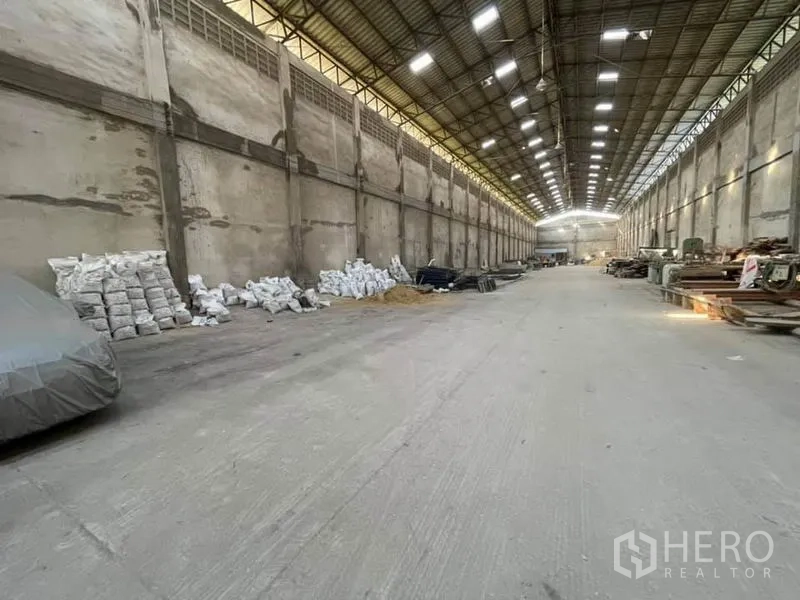 Warehouse for rent in Phra Samut Chedi, Samut Prakan - Long concrete-floored storage hall with materials stacked along the walls.