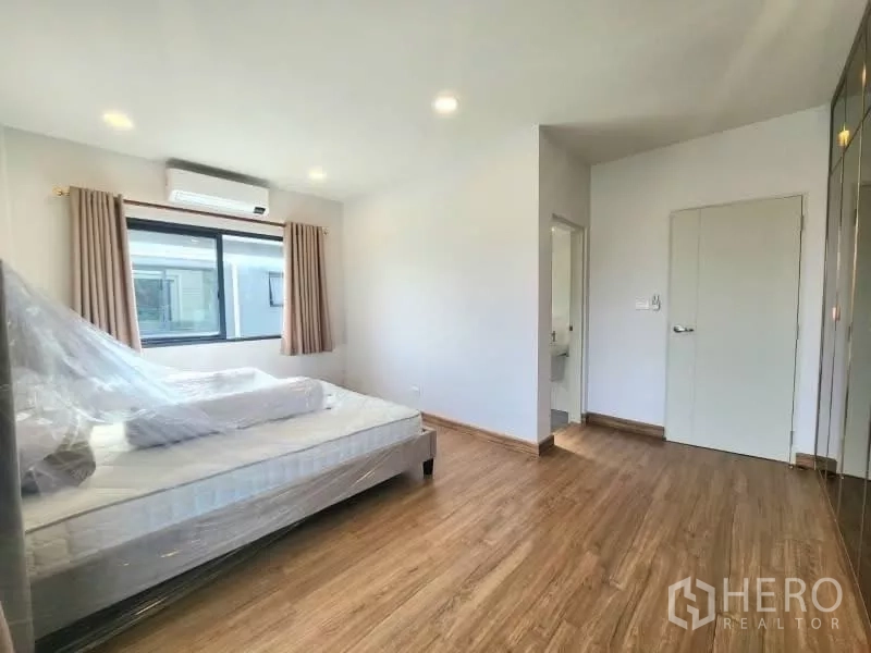 Detached House for rent in Bang Phli, Samut Prakan - Master bedroom with wood floors, large window, ensuite access and built-in wardrobe.
