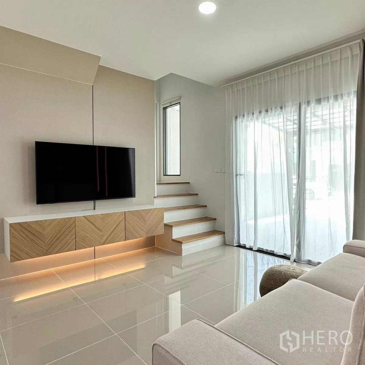 Townhouse for rent in Bang Phli, Samut Prakan - Bright living room with wall-mounted TV, floating cabinet, stairs and sheer curtains.