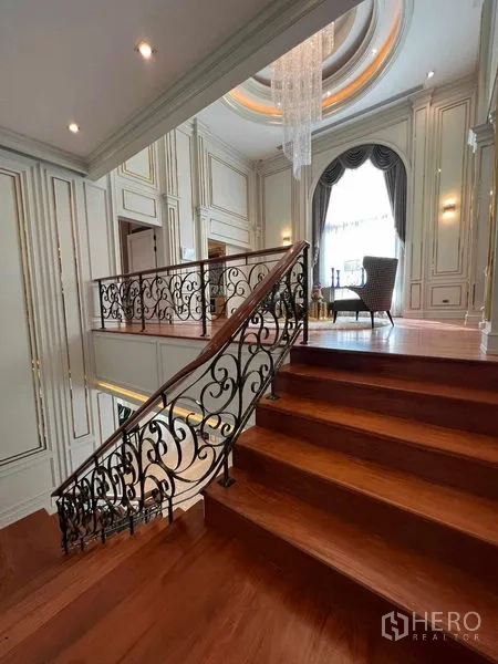 Detached House for rent or sale in Thawi Watthana, Bangkok - Ornate staircase with iron balustrade leading to a double-height hall.