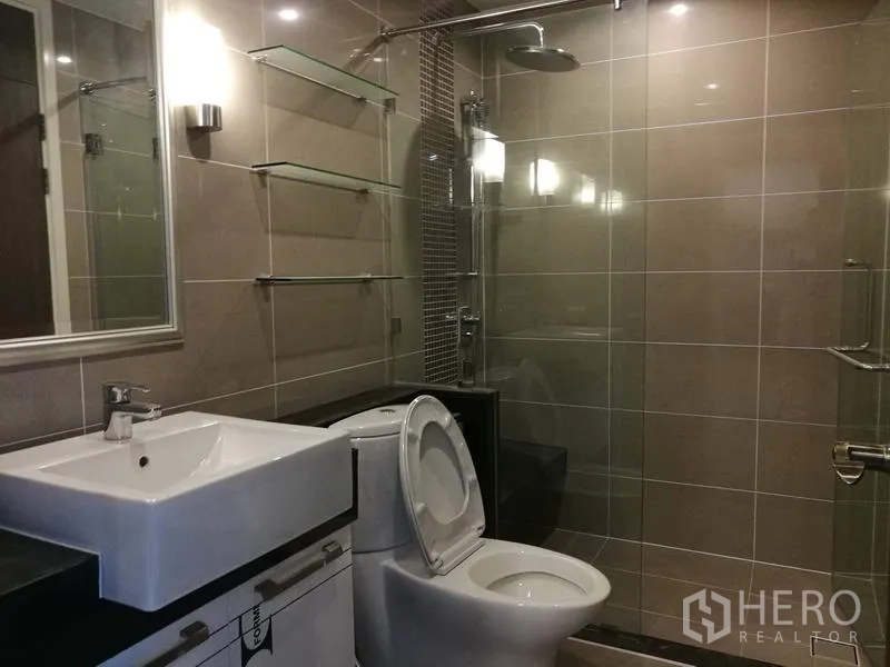 Condominium for rent in Sathon, Bangkok - Modern bathroom with glass-enclosed shower, rain showerhead, vanity sink and tiled walls.