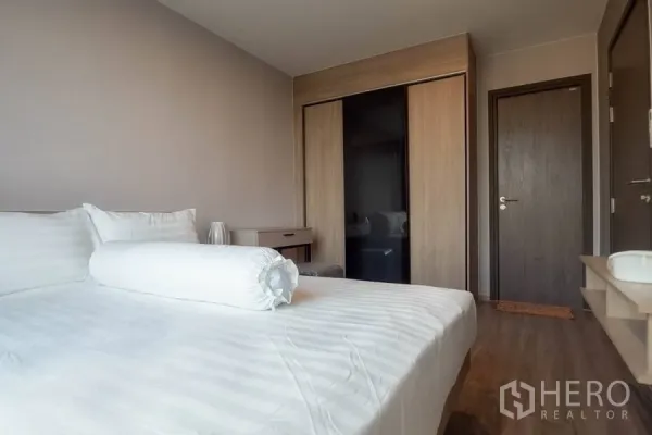 Condominium for rent or sale in Watthana, Bangkok - Cozy bedroom with queen bed, built-in sliding wardrobe, wood floors, and desk.