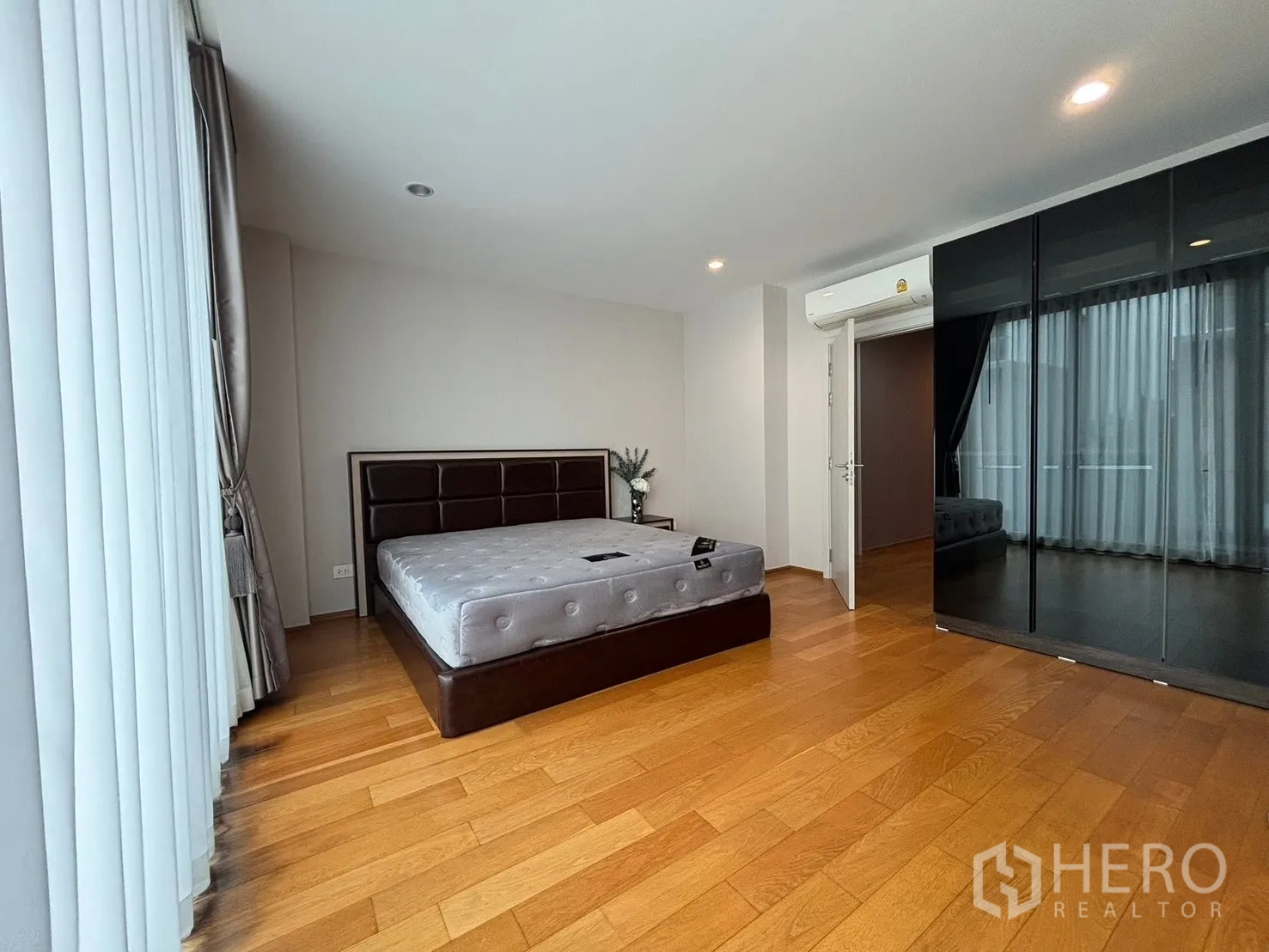 Townhouse for rent in Saphan Sung, Bangkok - Bedroom with brown upholstered bed, mirrored wardrobe, and drapes.