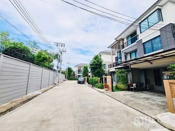 Detached House for sale in Suan Luang, Bangkok - Wide internal road lined with contemporary houses, utility poles, and landscaped plants.