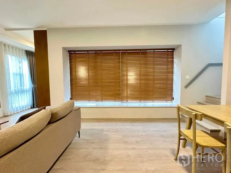 独立式住宅 出租或出售在Prawet, Bangkok - 餐区与楼梯旁的大窗，木百叶与浅色木地板。