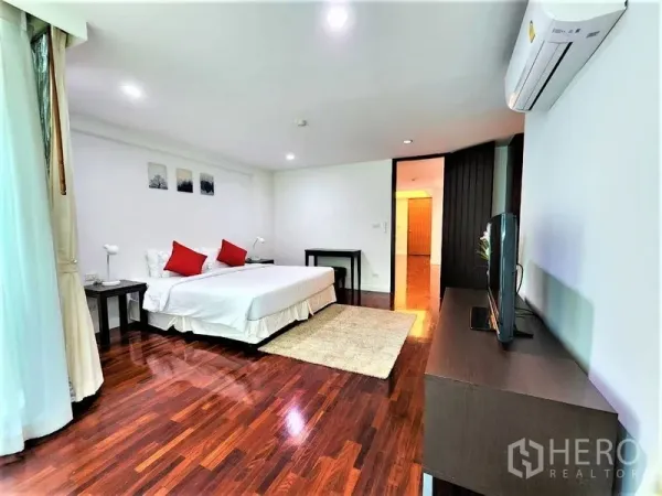 公寓 出租在Bang Rak, Bangkok - 主卧全景，白色墙面，分体空调，电视柜与深色木地板。