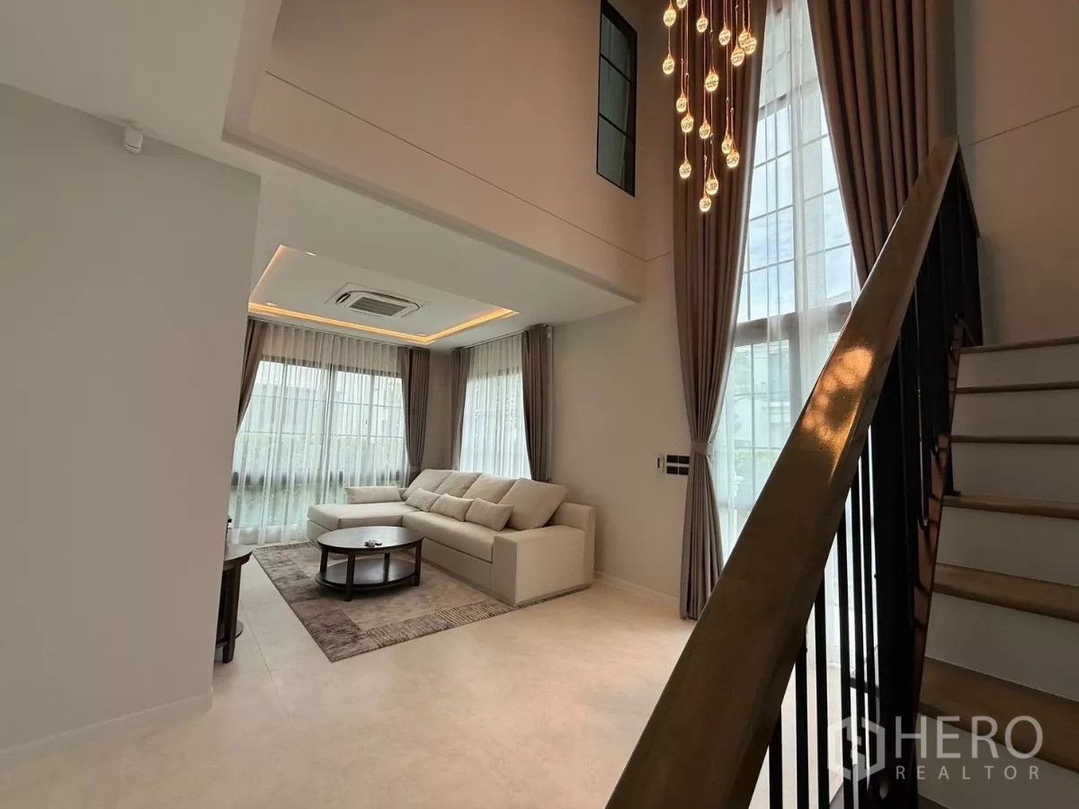 独立式住宅 出租或出售在Bang Phli, Samut Prakan - 挑高客厅，落地窗、吊灯与楼梯形成通透空间。