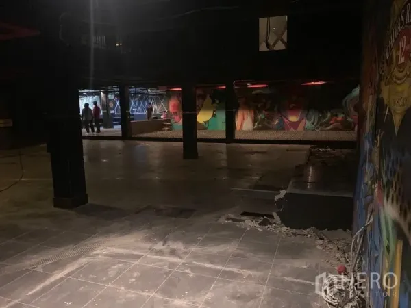 店屋 出租在Watthana, Bangkok - 开阔的工业风大厅，瓷砖地面、结构立柱和彩色涂鸦墙。