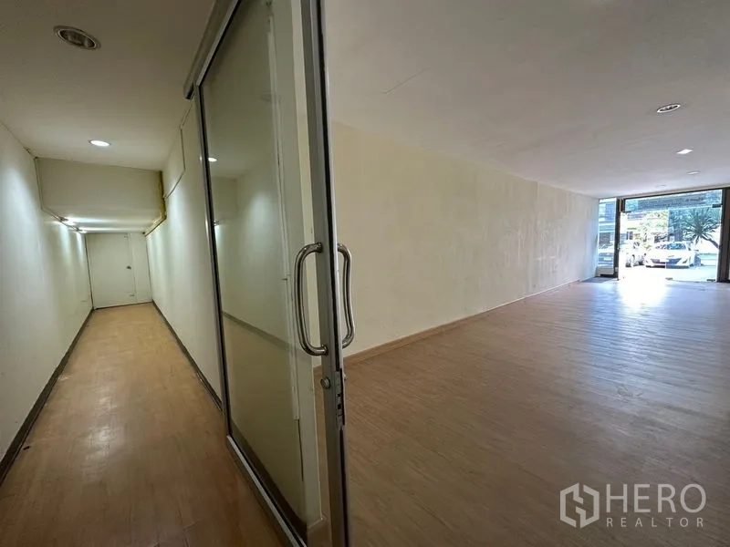 Warehouse for rent in Suan Luang, Bangkok - Long retail-ready hall with glass door leading to a bright street-facing space.