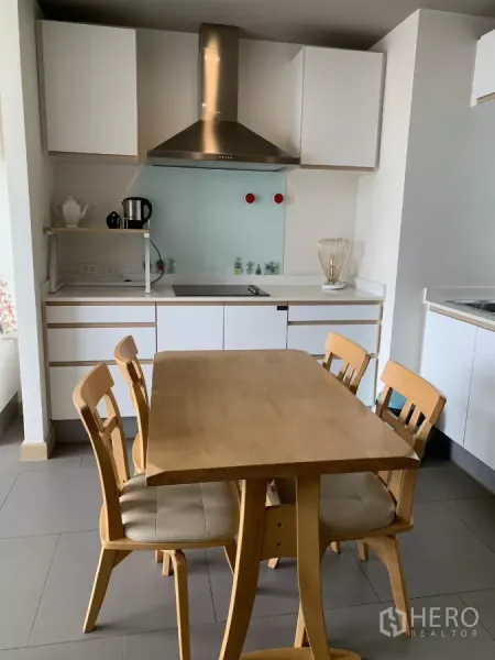 公寓 出租在Watthana, Bangkok - 现代小厨房，电磁炉与不锈钢烟机，木质餐桌四椅